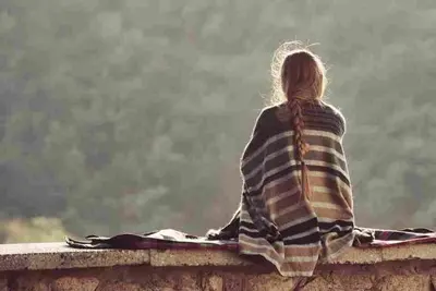 Person wrapped in a striped blanket sitting outdoors and facing a distant landscape