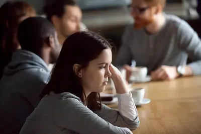 Person sits at a café table with several people blurred in the background