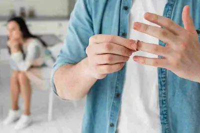 Person removes a ring while another person sits blurred in the background