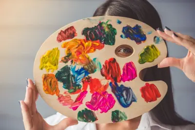 Person holds a paint-covered artist palette in front of their face