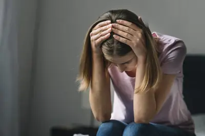 Person sits leaning forward with both hands on their head