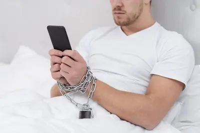 Person in bed holding a smartphone with chained wrists and a padlock