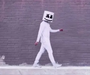 Person in white walking beside a brick wall with a smiling cube helmet