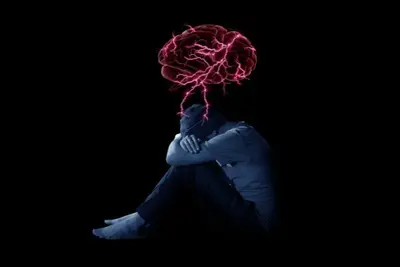 Seated figure with knees drawn up beneath a glowing brain graphic