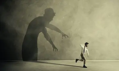 Small running figure moves away from a large reaching shadow on a wall