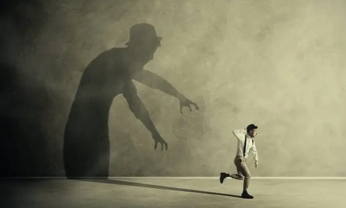 Small running figure moves away from a large reaching shadow on a wall