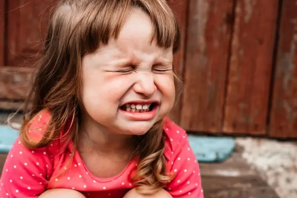 Young child sitting outdoors with eyes shut and teeth clenched