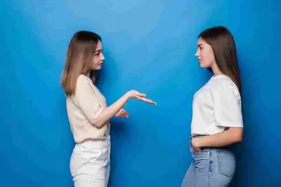 Two people stand facing each other as one gestures with an open hand
