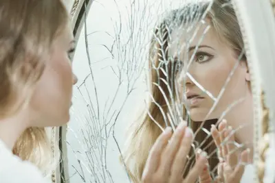 Person touches a cracked mirror while looking closely at their reflection