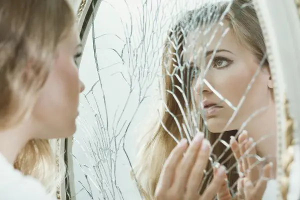 Person touches a cracked mirror while looking closely at their reflection