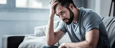 Person leans forward on a sofa with one hand resting on their head