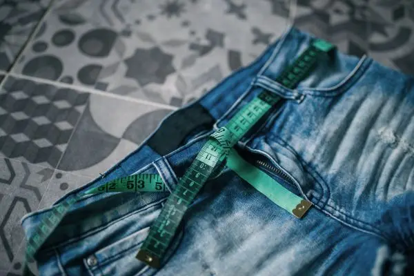 Measuring tape draped across a pair of jeans on a patterned floor